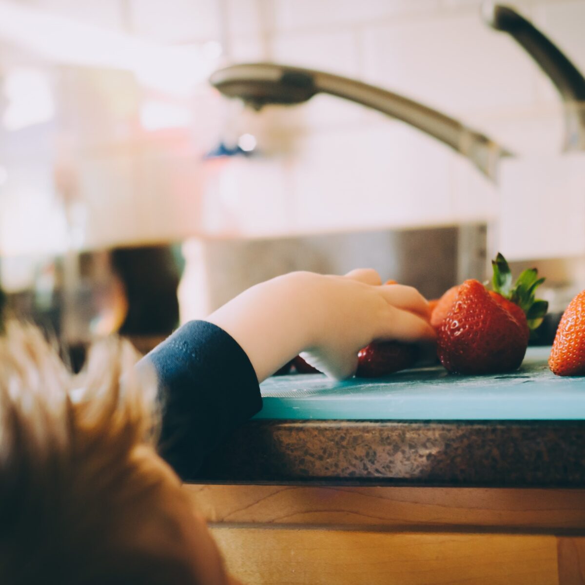Ein Kind greift in der Küche nach Erdbeeren