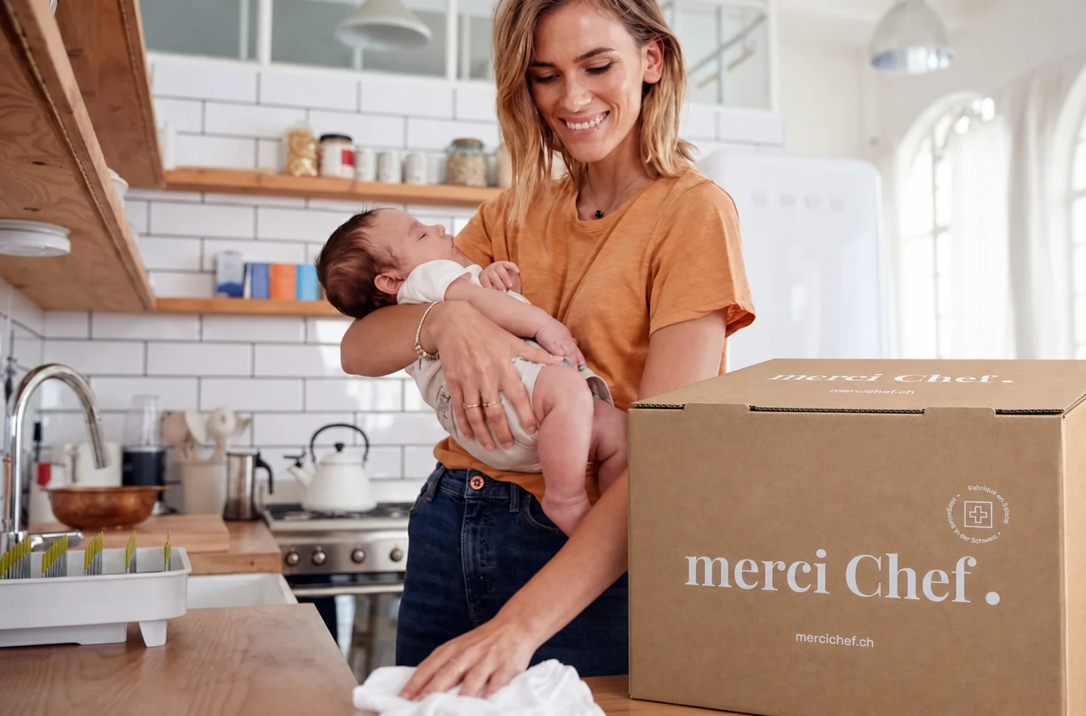 Ein Elternteil mit Baby und einer merciChef Lieferung in der Küche